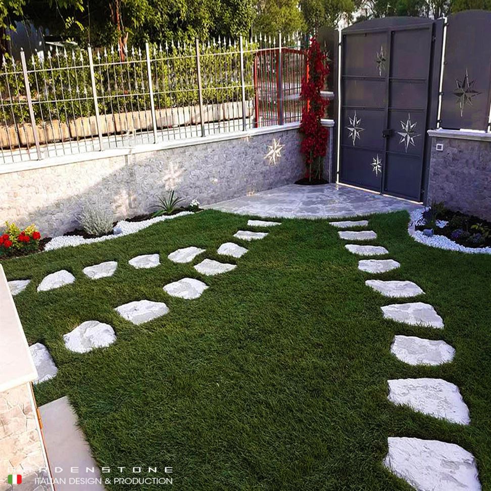 Camminamenti in finta pietra irregolari distanziati tra loro che conducono dal cancello all'entrata della casa, passando dal giardino